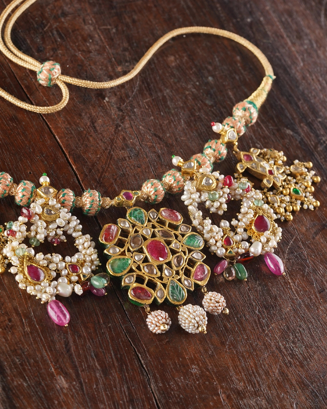 Handcrafted gold polki tukdi necklace featuring a floral pendant, pearl clusters, ruby and emerald accents, nath and fish motifs, fungar detailing, and traditional patwa threadwork.