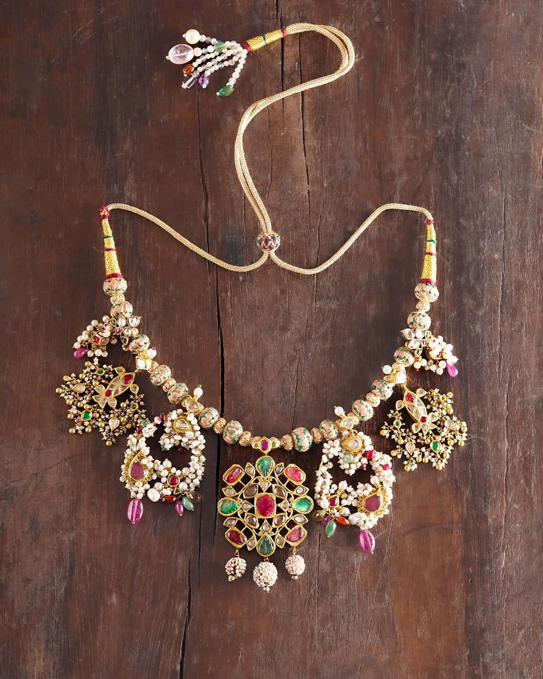 Handcrafted gold polki tukdi necklace featuring a floral pendant, pearl clusters, ruby and emerald accents, nath and fish motifs, fungar detailing, and traditional patwa threadwork.