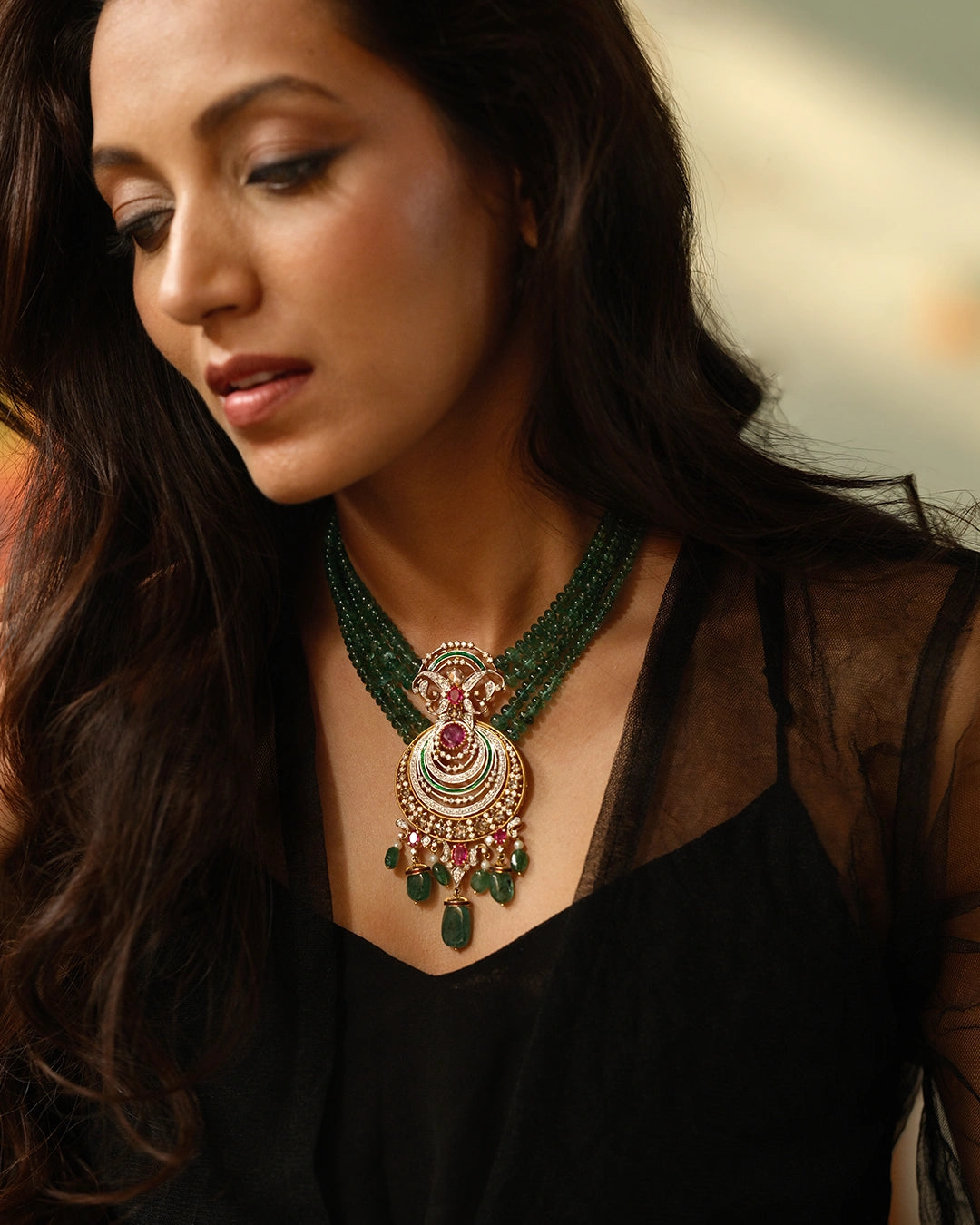 Model wearing the Aurus Jewels Zyar Necklace - a gold crescent pendant necklace with emerald bead strands, ruby, and cultured pearl drops, styled as a statement neckpiece