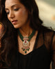 Model wearing the Aurus Jewels Zyar Necklace - a gold crescent pendant necklace with emerald bead strands, ruby, and cultured pearl drops, styled as a statement neckpiece